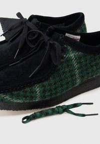 Scarpe con motivo verde e nero realizzate in lana infeltrita con accenti in suede; includono lacci neri e un laccio coordinato con motivo verde.