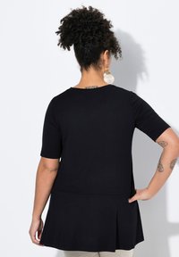 Mustat lyhythihaiset tunikat, joissa on levenevä helma ja pehmeä kangas. Ominaisuuksiin kuuluu pyöreä kaula-aukko ja hillityt laskokset, käytetään vaaleiden housujen päällä.