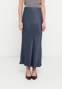 Satīna, tumši zila maksi svārki ar plūstošu siluetu, ar pieguļošu jostasvietu un gludu tekstūru. Kopā ar norāda burgundijas krāsas augstpapēžu kurpēm.