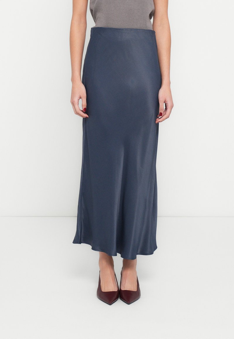 Satīna, tumši zila maksi svārki ar plūstošu siluetu, ar pieguļošu jostasvietu un gludu tekstūru. Kopā ar norāda burgundijas krāsas augstpapēžu kurpēm.