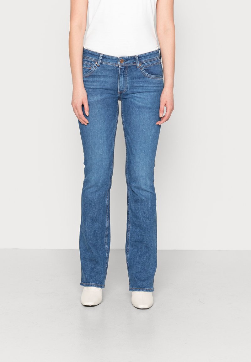 Vaqueros de mezclilla azul con un diseño de pierna recta, estilo de cinco bolsillos y un ligero desgastado. Combinados con una camiseta blanca y botas de tobillo blancas.