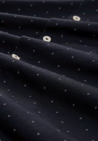 Marineblauer Stoff mit glatter Textur, der kleine weiße Würfelmuster aufweist und über Knopfverschlüsse an der Vorderseite verfügt, die gefaltete Abschnitte zeigen.
