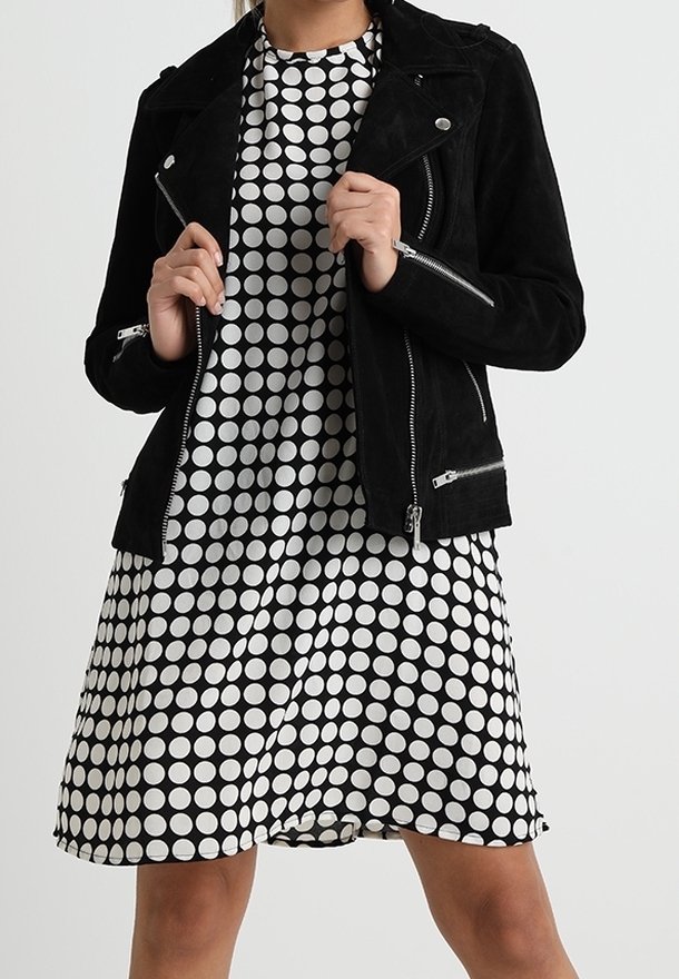 Svart mockabikerjacka med silverdragkedjor över en vit klänning med svarta prickar, korta ärmar och en utsvängd fåll.