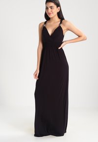 Vestido largo negro con tirantes finos, ajustado en la cintura, con un escote en V profundo y tejido suave y ligero.