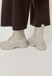 Botines beige de ante texturizado con punta redonda, tacón grueso, cordones en la parte frontal y cremallera lateral.