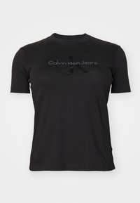 Melns īsām piedurknēm T-krekls, izgatavots no kokvilnas. Uz krūtīm ir spīdīga "CK" logo un diskrēta "Calvin Klein Jeans" uzraksta apdruka.