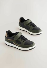 Baskets de sport noires et vertes avec une finition texturée, dotées d'une sangle Velcro, d'un design à lacets et d'une semelle intermédiaire blanche avec une semelle extérieure en caoutchouc.