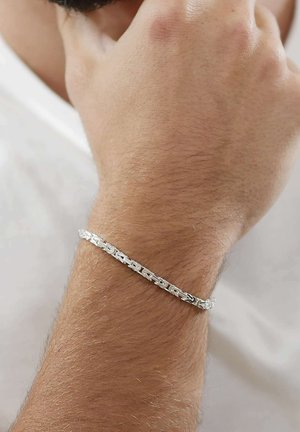 Close-up of a wrist wearing a silver chain bracelet with a distinct interlocking link design on light skin.