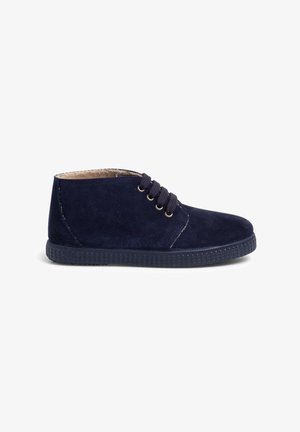 Botine din suede bleumarin, cu vârful rotund, talpă din cauciuc texturat și patru ochiuri pentru sireturi. Design simplu cu detalii de cusătură.