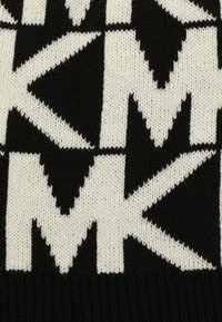 Tessuto a maglia bianco e nero con un motivo geometrico ripetuto di forme alternate a "M" e stelle. Texture morbida con orlo a coste.