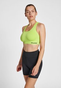 Neonowa zielona sportowa bielizna z bezszwowym designem. W zestawie z czarnymi szortami o wysokim stanie z małym logo z boku. Gładka tekstura.