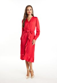 Abito in satin rosso con scollatura a V, maniche lunghe e orlo arricciato. Presenta una cintura in vita e un design fino al ginocchio. Indossato con tacchi dorati con cinturini.