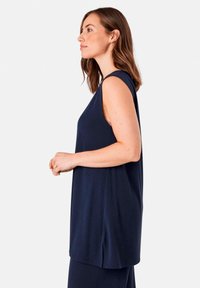 Marineblaue ärmellose Bluse mit lockerem Schnitt, weichem Stoff und seitlichem Schlitzdetail. Das Design weist einen runden Ausschnitt und minimale Nähte auf.