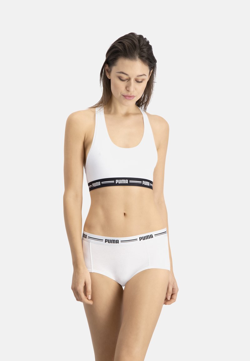 Sostén deportivo blanco con banda negra que presenta el logo "PUMA", combinado con ropa interior blanca a juego con cinturilla negra. Tejido suave, diseño ajustado.