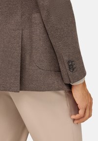 Brun strukturerad kavaj med notched krage, enkel bakventilation och detaljer med tre knappar på ärmarna, ihop med beiga byxor.