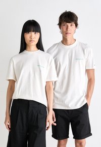 White cotton t-shirts with short sleeves and a crew neck; features a small turquoise logo on the left chest. Black loose-fitting pants and shorts.