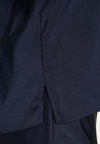 Blusa blu navy realizzata in tessuto liscio, con un'emivita leggermente curvata e una piccola apertura laterale per un tocco di dettagli e movimento.