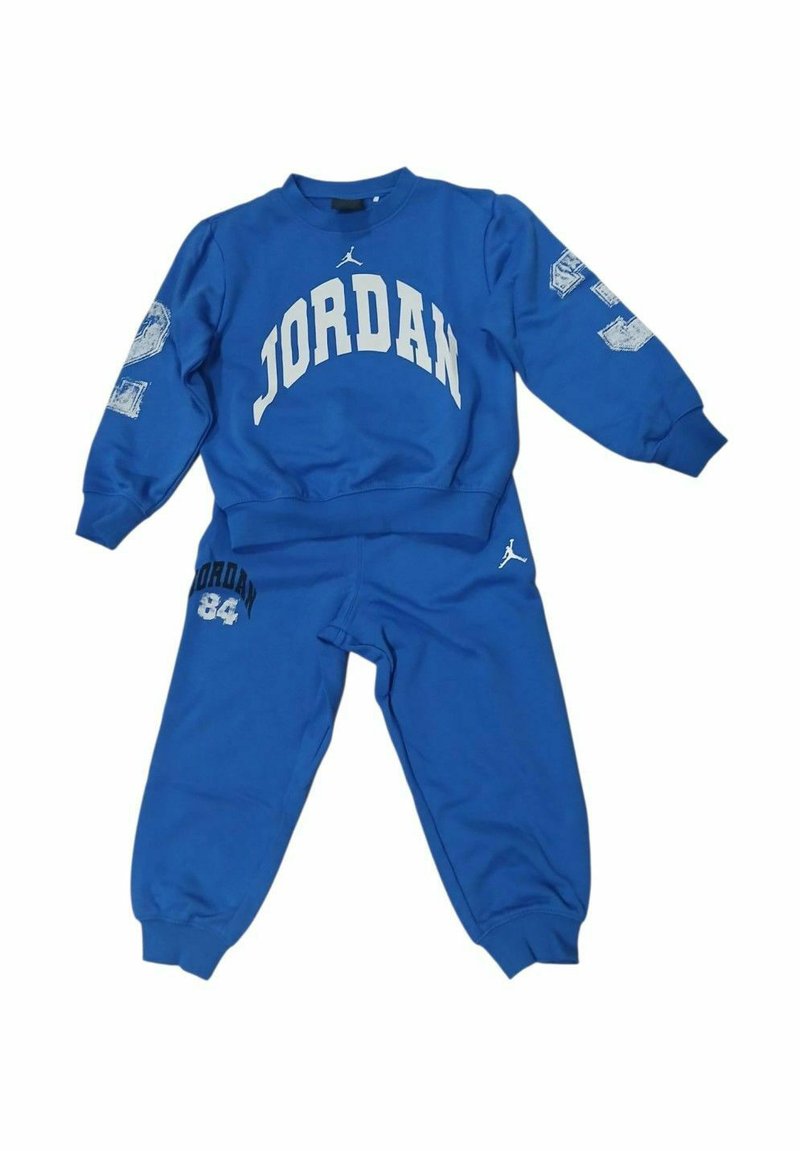 Tuta sportiva blu in cotone. Presenta la scritta "JORDAN" in bianco sulla parte superiore, con un logo e il numero "84" sui pantaloni. Tessuto liscio.
