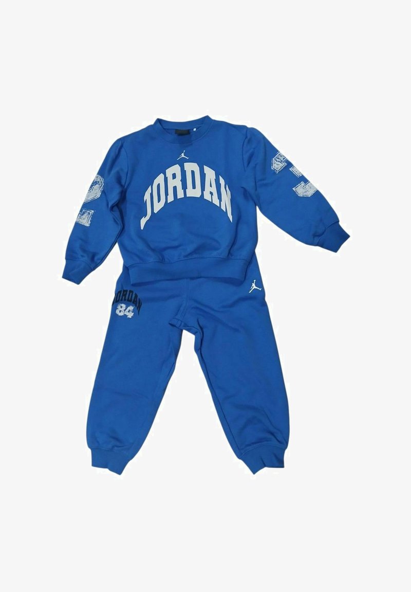 Tuta sportiva blu in cotone. Presenta la scritta "JORDAN" in bianco sulla parte superiore, con un logo e il numero "84" sui pantaloni. Tessuto liscio.