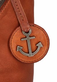 Étiquette en cuir marron avec un emblème métallique d'ancre, des bords cousus et un attache en cuir. Surface texturée avec une finition mate.