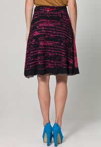 Gonna nera con motivi in script rosa, forma a A e uno strato inferiore in mesh nero. Abbinata a scarpe con tacco alto blu.