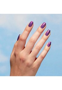 Paarse metallic nagellak aangebracht op lange, ovaalvormige nagels met een gladde textuur, weergegeven tegen een lichtblauwe achtergrond.