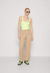 Neon grønn body med firkantet hals, beige vide bukser, svarte og grønne treningssko og hvite solbriller. Glatt stoff og skreddersydd passform.