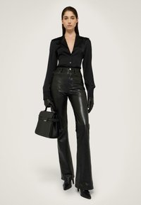 Černá blůza s špičatým límcem, zapínání na knoflíky a dlouhými rukávy, spárovaná s vysokým pasem, lesklými černými koženými zvonovými kalhotami. Černá kabelka.