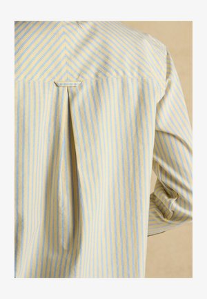 Dos d’une chemise rayée verticalement jaune et bleue avec un pli creux central et une petite boucle en tissu sous la couture du yoke.