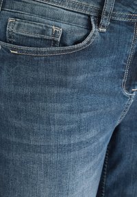 Vaqueros de mezclilla en un tono azul medio que presentan una superficie texturizada, corte clásico, bolsillos estándar y detalles de costura visibles.