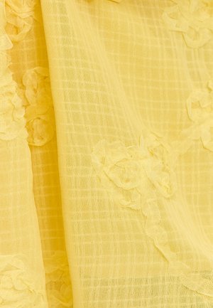 Gelbes strukturiertes Gewebe mit einem Gittermuster und floralem Applikationsmuster entlang einer Kante. Das Material wirkt leicht und durchsichtig.