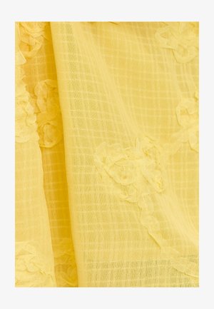 Geel textiel met een rasterpatroon en bloemapplicaties langs één rand. Het materiaal lijkt licht en doorschijnend.