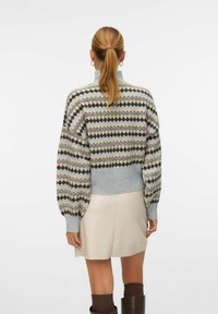 Gestrickter Pullover in Hellgrau, mit einem Rautenmuster in Beige und Braun, Ballonärmel und einem gerippten Saum. Kombiniert mit einem cremefarbenen Rock.