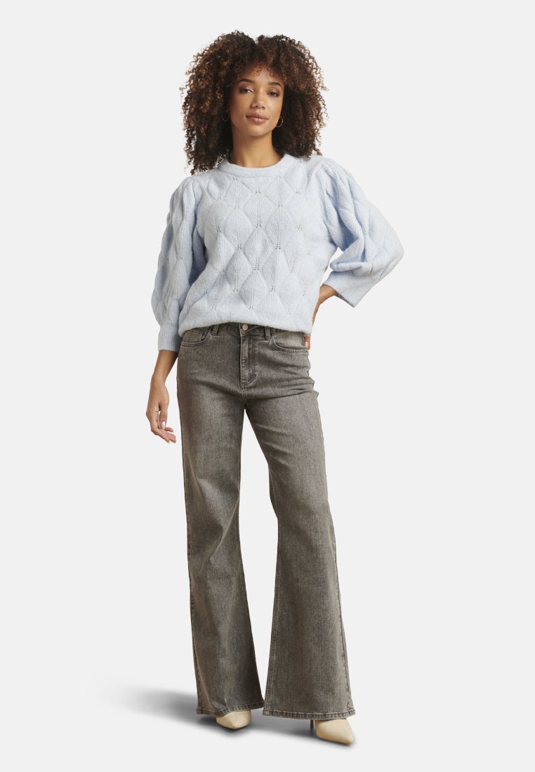 Light blue knitted sweater with diamond pattern and puffed sleeves, paired with gray flared jeans and beige pointed-toe shoes.