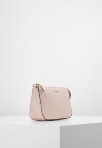 Borsa a tracolla in pelle rosa chiaro con superficie testurizzata, zip dorata e branding discreto sul davanti, con un design curvato.