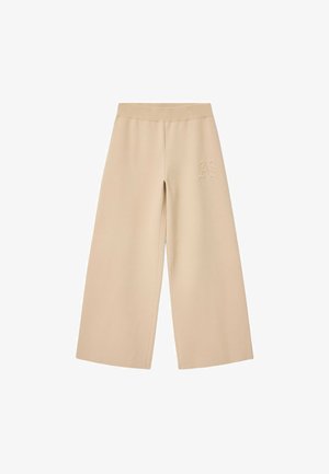 Beżowe szerokie spodnie dresowe wykonane z miękkiego materiału, z elastycznym paskiem w talii i wytłoczonym logo „AS” po bokach.