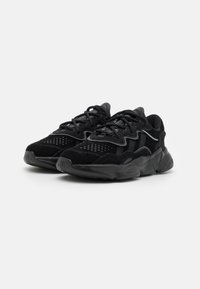 Black sneakers with a mix of suede and mesh materials, featuring a chunky sole, textured accents, and multi-layered design details.