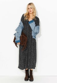 Robe maxi noire à motifs floraux, superposée avec une veste en denim bleu clair, un sac à main à franges marron et des bottines noires à talons. Texture lisse, coupe décontractée.
