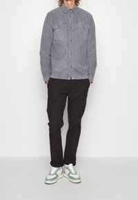 Gray denim shirt with long sleeves and two chest pockets, paired with black trousers and white sneakers featuring green accents.