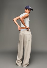 Hvid cropped top, grå vide sweatpants med forlommer og blå elastisk talje. Mørkeblå kasket. Model placeret sidelæns.