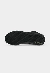 Čierna teniska Reebok zobrazená zo spodnej časti podrážky, s textúrovaným dezénom a logom Reebok blízko päty.
