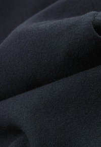 Černá vlněná tkanina s měkkým, texturovaným povrchem, který má jemné záhyby a sklady, zdůrazňující její silnou strukturu a teplost.