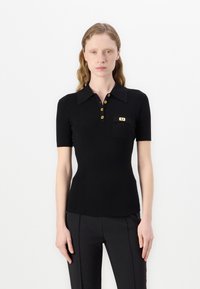 Polo noir à côtes avec col, manches courtes, boutons dorés et une petite poche sur la poitrine avec un accent métallique.