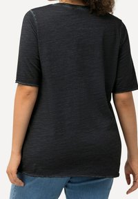 Černé tričko s krátkým rukávem, vyrobené z měkké, texturované tkaniny a se zaobleným lemem. Nabízí volný střih, viditelné švy a detail s hrubým okrajem.