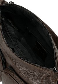 Interno di una borsa in pelle marrone con scomparti con cerniera, superficie testurizzata e rivestimento nero. Molti taschini per l'organizzazione.