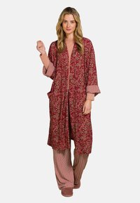 Long, red floral kimono with wide sleeves and pockets; paired with striped beige pants and soft brown slippers.