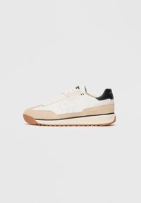 Sneaker bianco e beige con upper in suede e tessuto, accentuazione nera sul tallone, punta arrotondata e suola in gomma testurizzata con motivo zigzag.