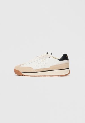 Sneaker bianco e beige con upper in suede e tessuto, accentuazione nera sul tallone, punta arrotondata e suola in gomma testurizzata con motivo zigzag.