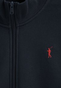 Felpa con zip di colore blu navy, dotata di un alto collo, texture a coste e un piccolo logo ricamato di un golfista rosso sul lato sinistro.