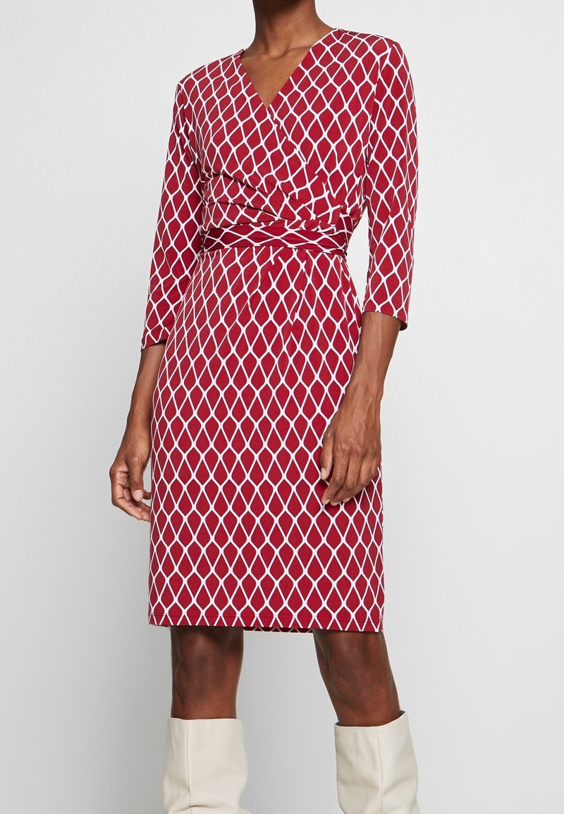 Robe rouge avec un motif de losanges blancs, présentant un design portefeuille et des manches trois-quarts, texture lisse, longueur au genou.